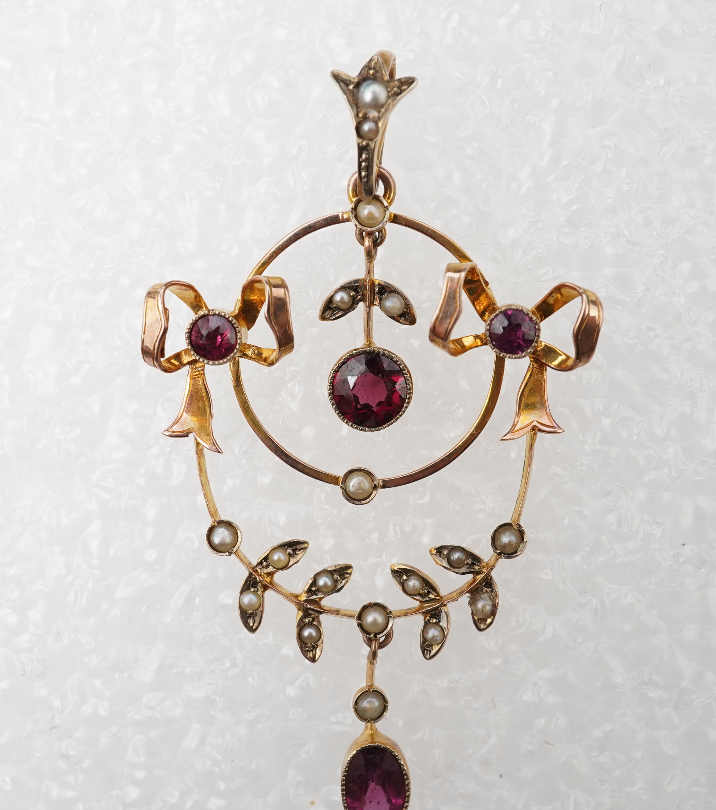 An Edwardian garnet and seed pearl pendant, early 20th century, of foliate design with ribbon bow motifs, set with circular-cut and oval garnets and seed pearls, mounted in gold, length 5.2cm, stamped 9CT, gross weight a